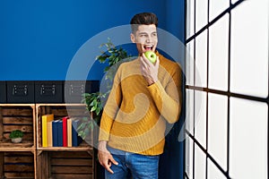 Young hispanic man smiling confident eating apple at home