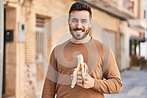 Young hispanic man smiling confident eating banana at street