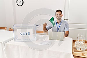 Young hispanic man smiling confident holding arabia saudi flag working at electoral college photo