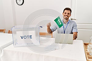 Young hispanic man smiling confident holding arabia saudi flag working at electoral college photo