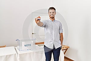 Young hispanic man smiling confident holding i voted badge at electoral college