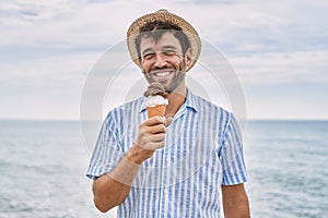 Young hispanic man smiling happy eating ice cream at the beach