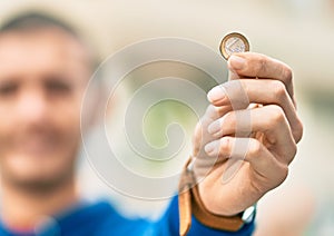 Young hispanic man smiling happy holding 1 euro coin at the city