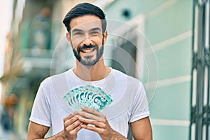 Young hispanic man smiling happy holding chinese yuan banknotes at the city
