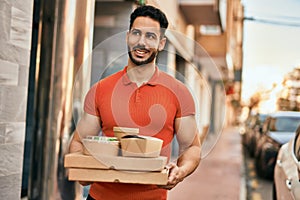 Young hispanic man smiling happy holding take away food at the city