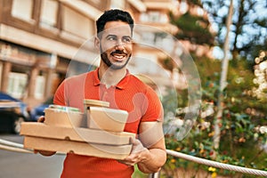 Young hispanic man smiling happy holding take away food at the city