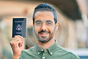 Young hispanic man smiling happy holding united states passport at the city