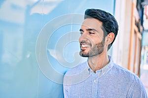 Young hispanic man smiling happy leaning on the wall at the city