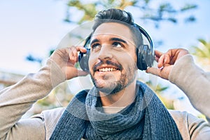 Young hispanic man smiling happy listening to music using headphones walking at the city