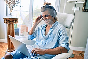 Young hispanic man smiling happy using laptop and headphones at home