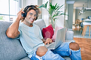 Young hispanic man smiling happy using laptop and headphones at home