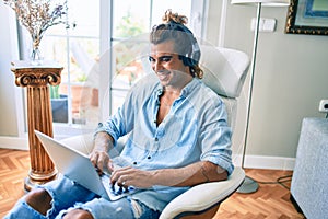 Young hispanic man smiling happy using laptop and headphones at home