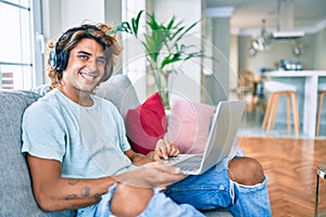 Young hispanic man smiling happy using laptop and headphones at home