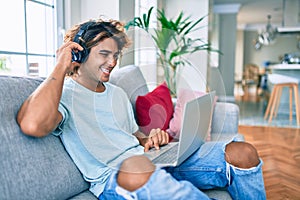 Young hispanic man smiling happy using laptop and headphones at home