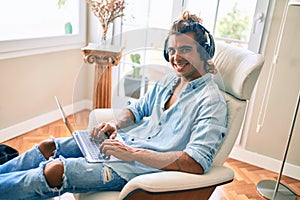 Young hispanic man smiling happy using laptop and headphones at home