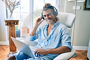 Young hispanic man smiling happy using laptop and headphones at home