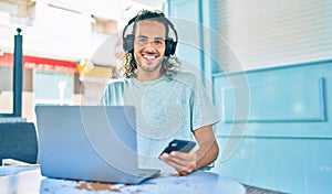 Young hispanic man smiling happy working using laptop and headphones at terrace of coffee shop