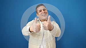 Young hispanic man smiling with thumbs up over isolated blue background