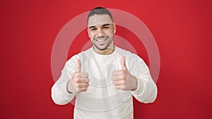 Young hispanic man smiling with thumbs up over isolated red background