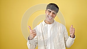 Young hispanic man smiling with thumbs up over isolated yellow background