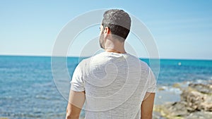 Young hispanic man standing backwards at the beach