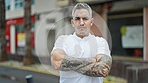 Young hispanic man standing with crossed arms and serious face at street