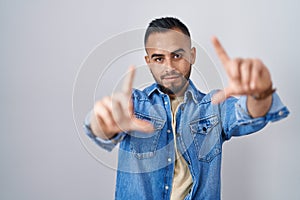 Young hispanic man standing over isolated background doing frame using hands palms and fingers, camera perspective