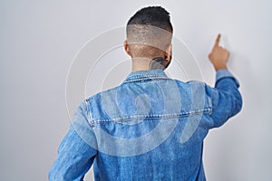 Young hispanic man standing over isolated background posing backwards pointing ahead with finger hand