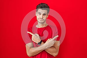 Young hispanic man standing over red background pointing to both sides with fingers, different direction disagree