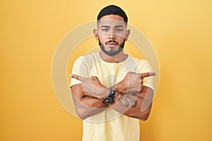 Young hispanic man standing over yellow background pointing to both sides with fingers, different direction disagree