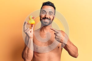 Young hispanic man standing shirtless holding duck toy smiling happy pointing with hand and finger