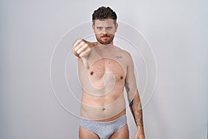 Young hispanic man standing shirtless wearing underware looking unhappy and angry showing rejection and negative with thumbs down