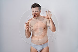 Young hispanic man standing shirtless wearing underware smiling funny doing claw gesture as cat, aggressive and sexy expression