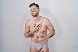 Young hispanic man standing shirtless wearing underware smiling and laughing hard out loud because funny crazy joke with hands on