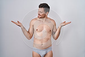 Young hispanic man standing shirtless wearing underware smiling showing both hands open palms, presenting and advertising