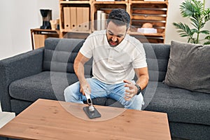 Young hispanic man stressed breaking smartphone with hammer at home