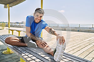 Young hispanic man stretching leg muscles outdoors