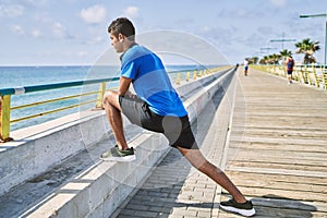 Young hispanic man stretching leg muscles outdoors