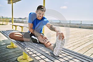 Young hispanic man stretching leg muscles outdoors