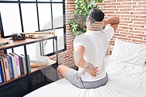 Young hispanic man suffering for back injury sitting on bed at bedroom