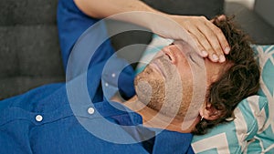 Young hispanic man suffering for headache lying on sofa at home