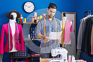 Young hispanic man tailor smiling confident reading document at sewing studio