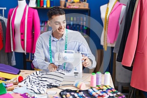 Young hispanic man tailor smiling confident using sewing machine at sewing studio