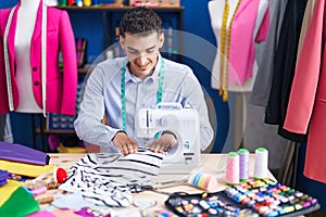 Young hispanic man tailor smiling confident using sewing machine at sewing studio