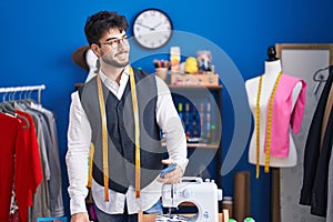 Young hispanic man tailor smiling confident using smartphone at sewing studio