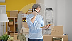 Young hispanic man talking on smartphone reading document smiling at new home