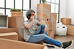 Young hispanic man talking on the smartphone sitting on the floor at new home