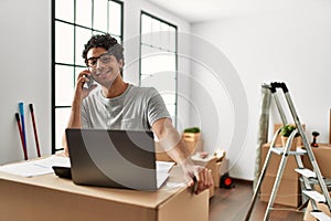Young hispanic man talking on the smartphone using laptop at new home