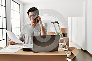 Young hispanic man talking on the smartphone using laptop at new home