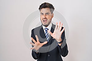 Young hispanic man with tattoos wearing business suit and tie afraid and terrified with fear expression stop gesture with hands,